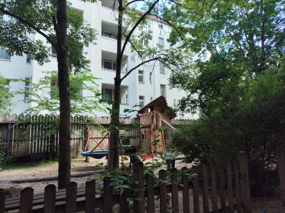Begrünter Außenspielplatz mit Nestschaukel und Holzspielhaus